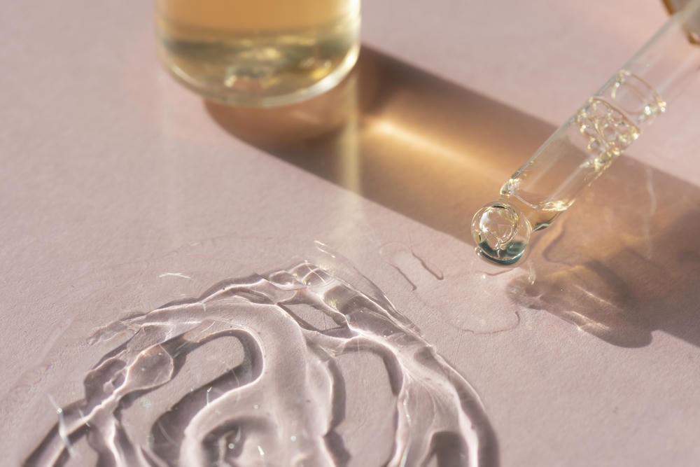 aha. Cận cảnh ống nhỏ giọt có serum dưỡng da mặt đổ trên nền màu hồng với bóng chai vàng cho dự án làm đẹp của bạn