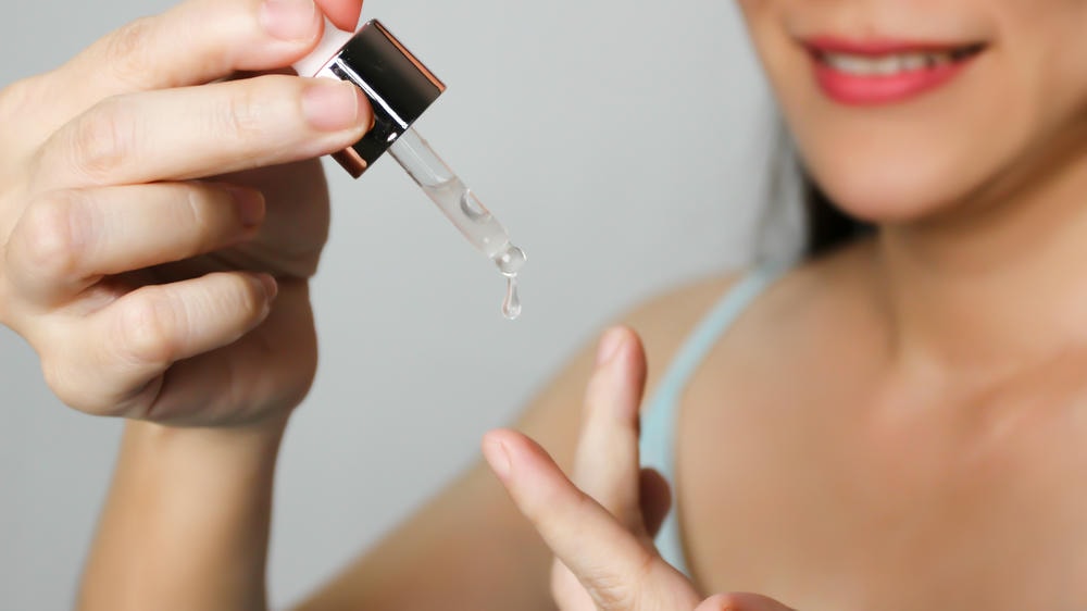 aha. Người phụ nữ châu Á xinh đẹp cầm ống nhỏ giọt nhỏ nước hoặc serum lên ngón tay Ống nhỏ giọt mỹ phẩm với giọt dầu Chăm sóc da và vẻ đẹp theo khái niệm