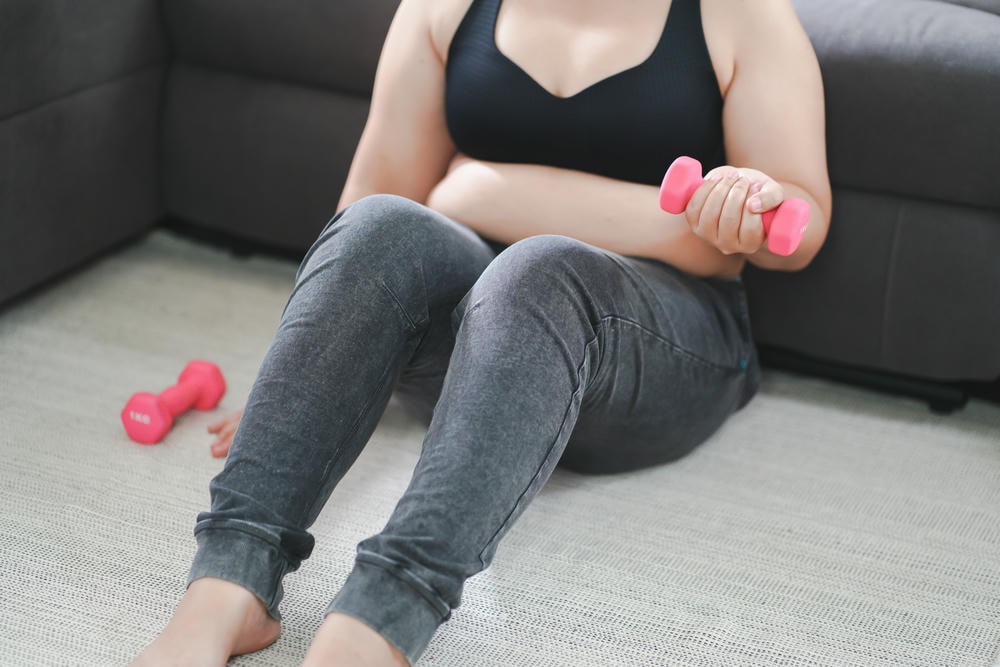 cách làm bụng nhỏ sau sinh tại nhà. Người phụ nữ thừa cân tập thể dục để giảm cân tập thể dục với tạ ở tư thế kéo giãn tại nhà trong phòng khách Người phụ nữ béo vui vẻ ăn kiêng khái niệm lối sống lành mạnh