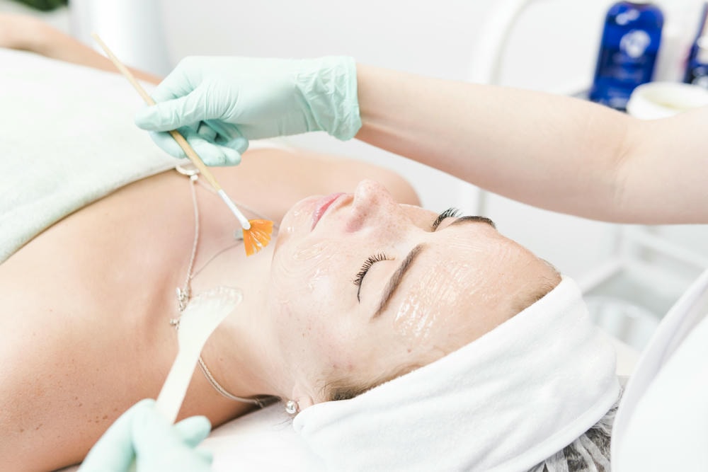 chemical peel. Chuyên gia thẩm mỹ thoa đều gel lên mặt bệnh nhân bằng cọ