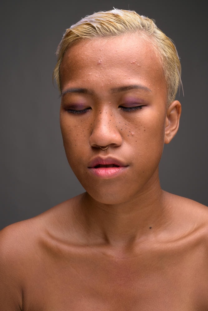 da không đều màu. Ảnh chụp trong studio của một phụ nữ trẻ đẹp nổi loạn với mái tóc ngắn trên nền xám