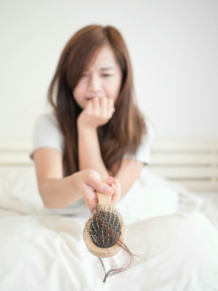 giảm rụng tóc. Người phụ nữ buồn bã cầm lược với tóc rụng trên giường tại nhà