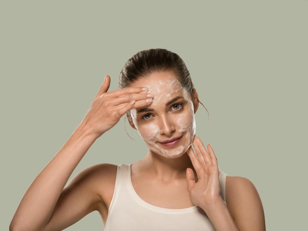 sữa rửa mặt da dầu mụn. Người phụ nữ rửa mặt bằng xà phòng, làm sạch da. Nền màu. Xanh lục