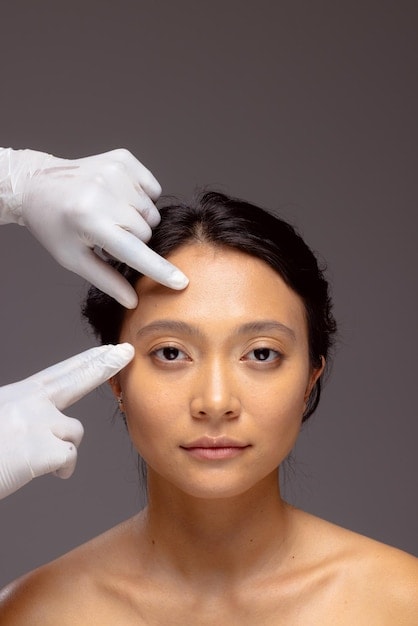 tái tạo da. Bàn tay của chuyên viên thẩm mỹ đeo găng tay phẫu thuật màu trắng chạm vào mặt người phụ nữ châu Á với mái tóc đen, khoảng trống để sao chép
