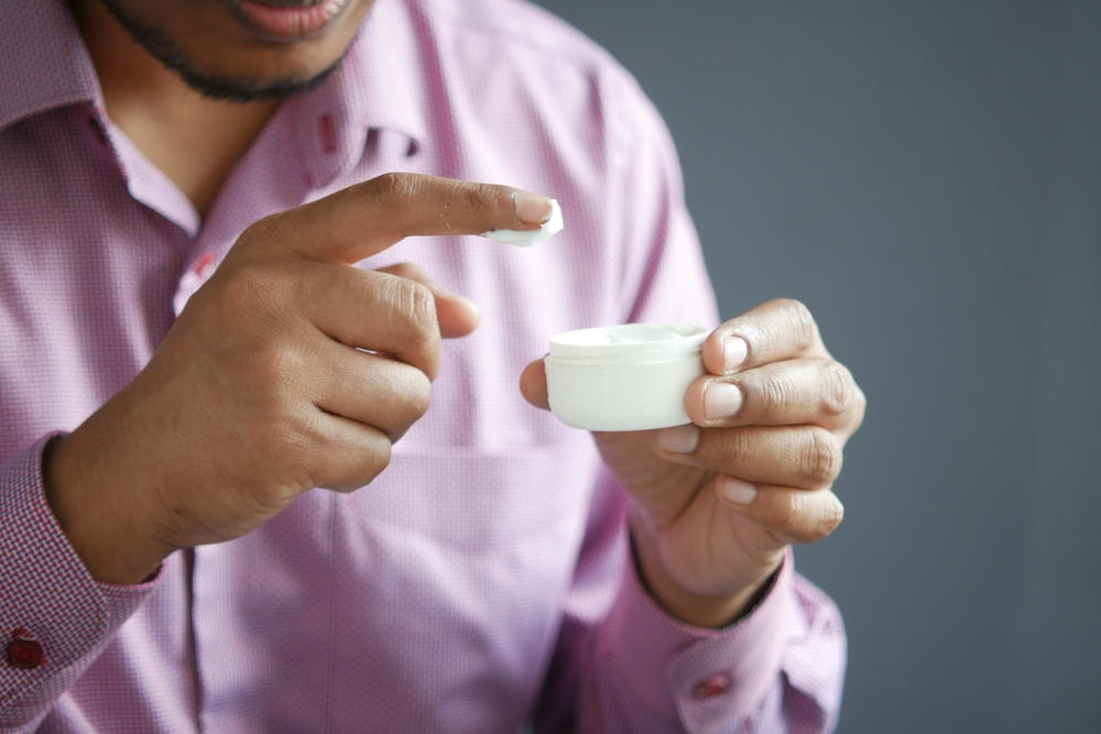 thuốc bôi corticoid. Người đàn ông thoa kem dưỡng da lên da