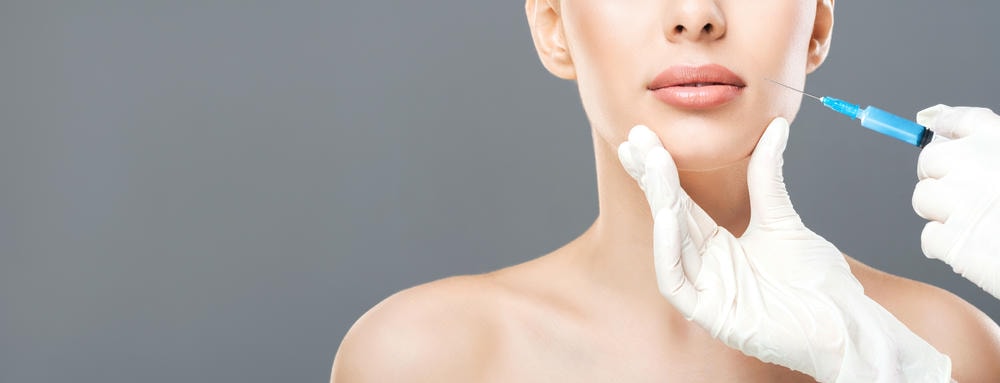 tiêm botox gọn hàm bao lâu thì gọn. Quy trình làm đẹp người phụ nữ trẻ bán khỏa thân đang được tiêm nâng cơ da mặt trên nền xám