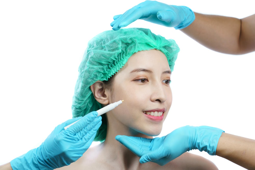 tiêm botox là gì. Bàn tay của chuyên viên thẩm mỹ vẽ đường trên khuôn mặt người phụ nữ châu Á để phẫu thuật thẩm mỹ.
