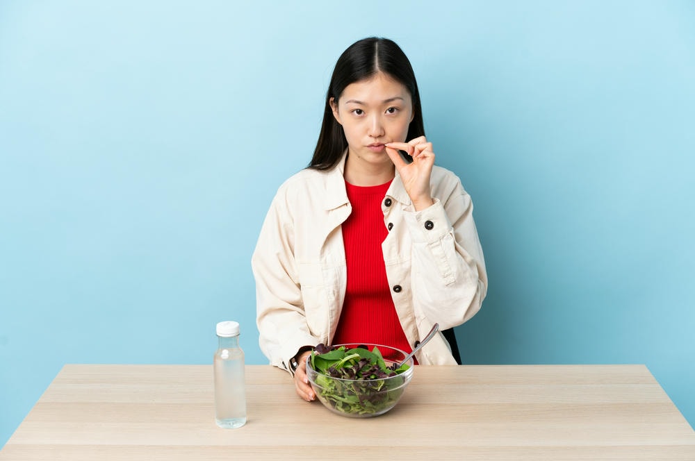 tiêm filler cần kiêng gì. Cô gái Trung Quốc trẻ tuổi ăn salad thể hiện dấu hiệu im lặng