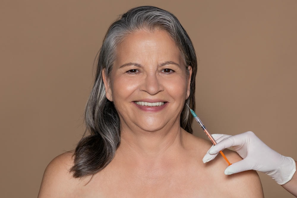 tiêm filler có bị chảy xệ không. Người phụ nữ lớn tuổi tóc hoa râm người châu Âu mỉm cười tận hưởng quy trình làm đẹp, chuyên gia thẩm mỹ thực hiện tiêm