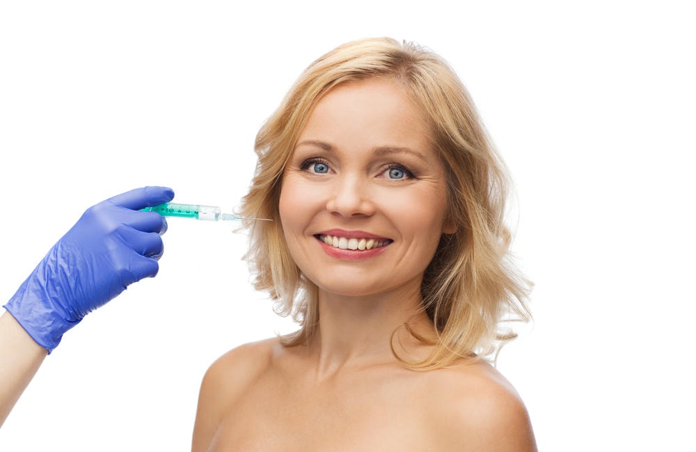 tiêm filler rãnh cười. Khái niệm về phẫu thuật thẩm mỹ chống lão hóa, vẻ đẹp - khuôn mặt người phụ nữ mỉm cười và bàn tay của chuyên gia thẩm mỹ đeo găng tay với ống tiêm tiêm vào má