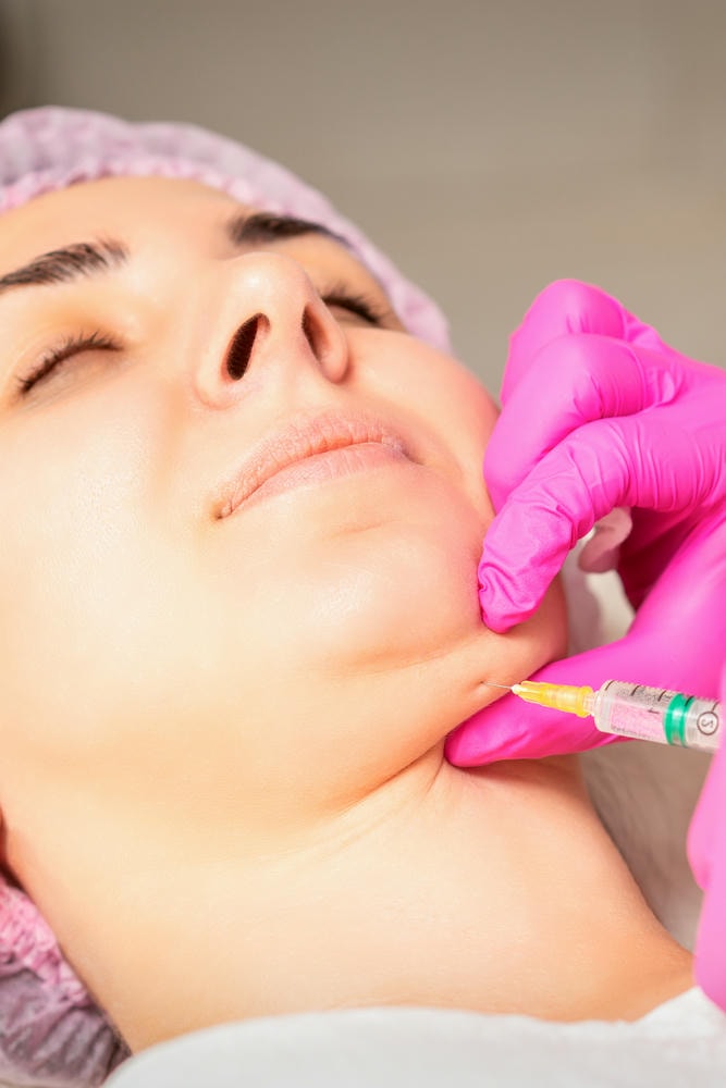 tiêm nọng cằm. Chuyên gia thẩm mỹ tiêm tan mỡ vào cằm của một phụ nữ trẻ để chống lại nọng cằm trong thẩm mỹ viện.