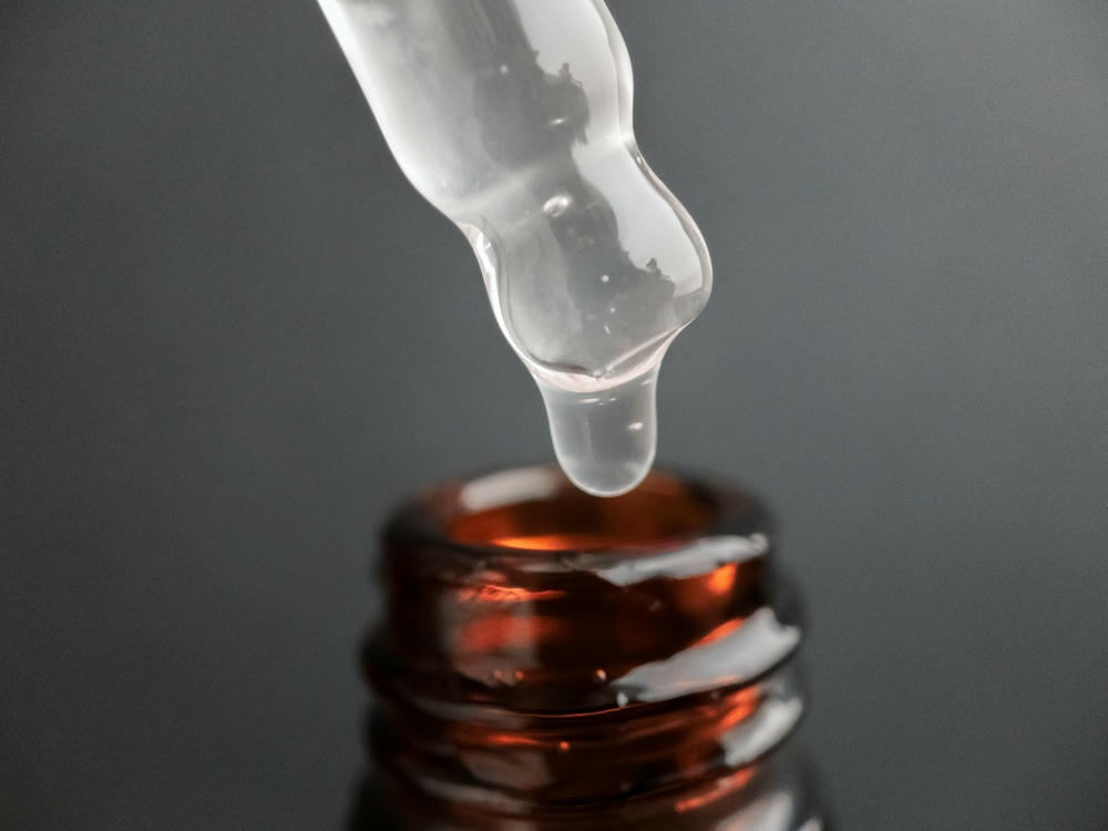 tranexamic acid là gì. Ống nhỏ giọt có một giọt huyết thanh hoặc dầu cho mặt và axit hyaluronic trên nền đen tuyệt đẹp, cận cảnh. Khái niệm làm đẹp.