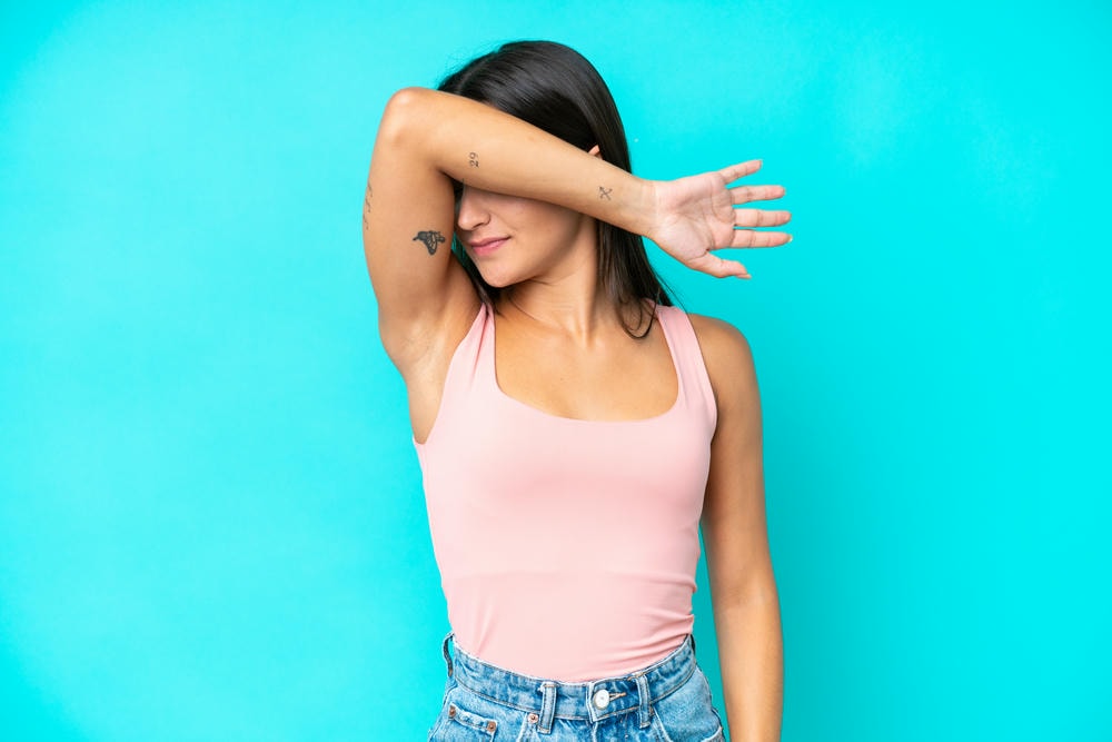 trị thâm nách. Người phụ nữ da trắng trẻ tuổi cô lập trên nền xanh che mắt bằng tay